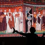 An art history professor lecturing in front of a large projection of the Parthenon on the Athenian Acropolis.