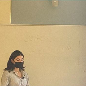 A masked teacher in front of a whiteboard in a classroom.