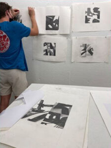 A student in a blue shirt pinning drawings to a classroom wall.
